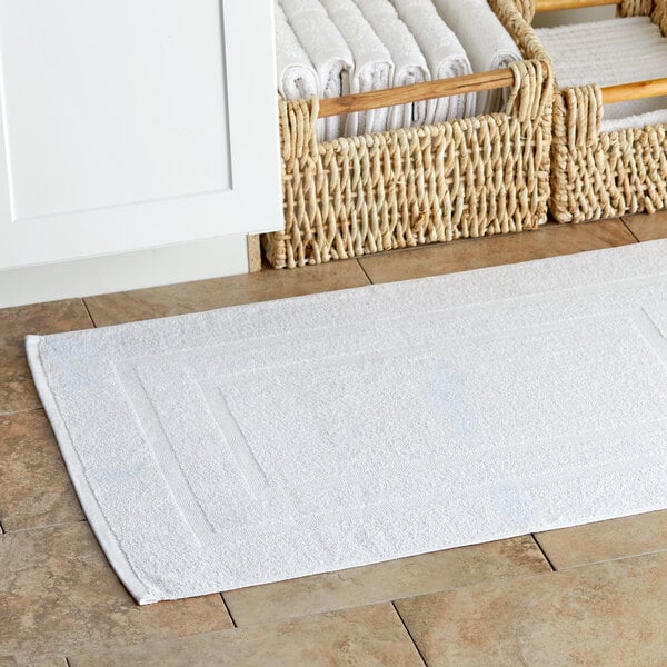 A white Lavex bath mat on a tile floor next to baskets.