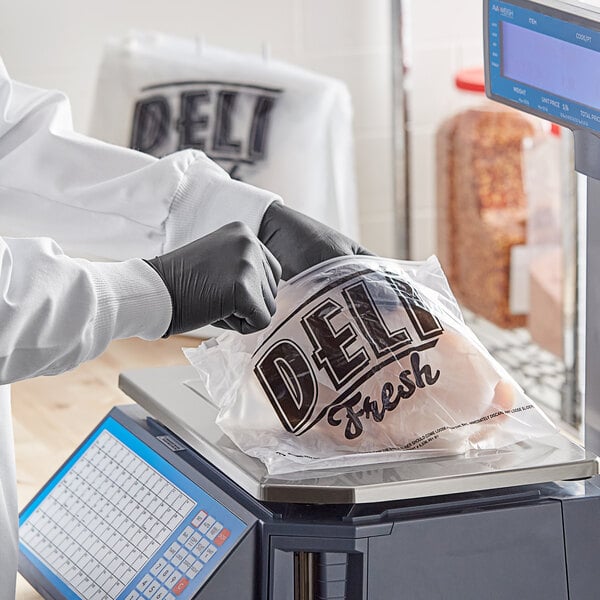 A person in gloves using a Choice Deli Saddle Bag Stand to weigh chicken and place it in a printed "Deli Fresh" plastic bag.