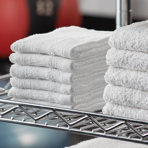 A metal rack with a stack of Lavex white cotton washcloths.
