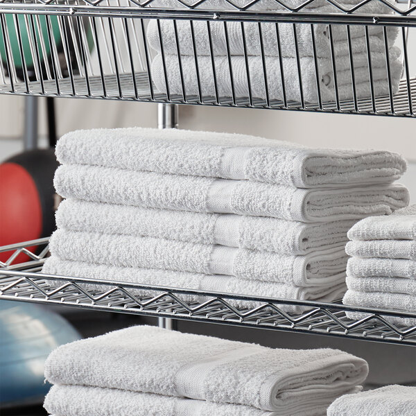 A stack of Lavex white bath towels on a metal shelf.