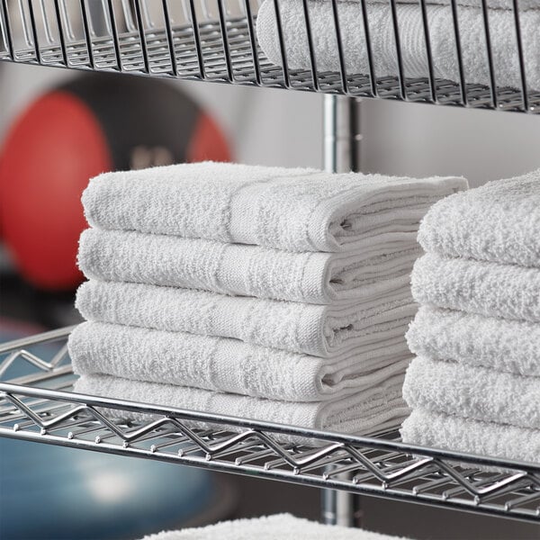 A metal rack with a stack of white Lavex cotton hand towels.