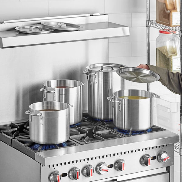A man standing in front of a stove with a Choice aluminum stock pot on it.