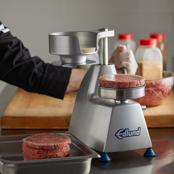 A person using an Edlund machine to make round hamburger patties on a counter.