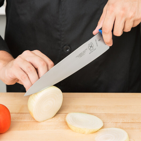 A person using a Mercer Culinary Millennia Colors chef knife to slice an onion.