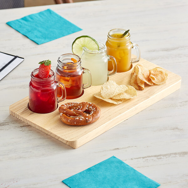 An Acopa natural wood flight tray with mini drinking jars filled with drinks and snacks on a table.