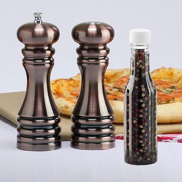 A Chef Specialties burnished copper pepper mill and salt shaker on a table with pizza.