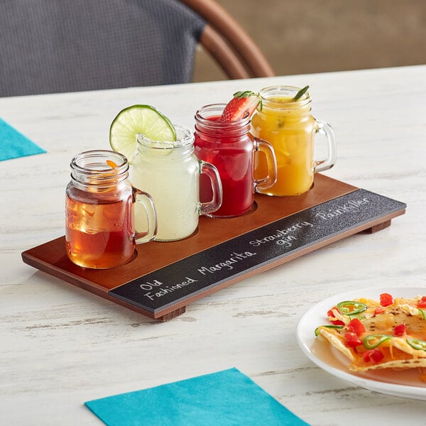 A table with an Acopa Write-On Flight Tray with drinks in mini glass jars and a plate of food.