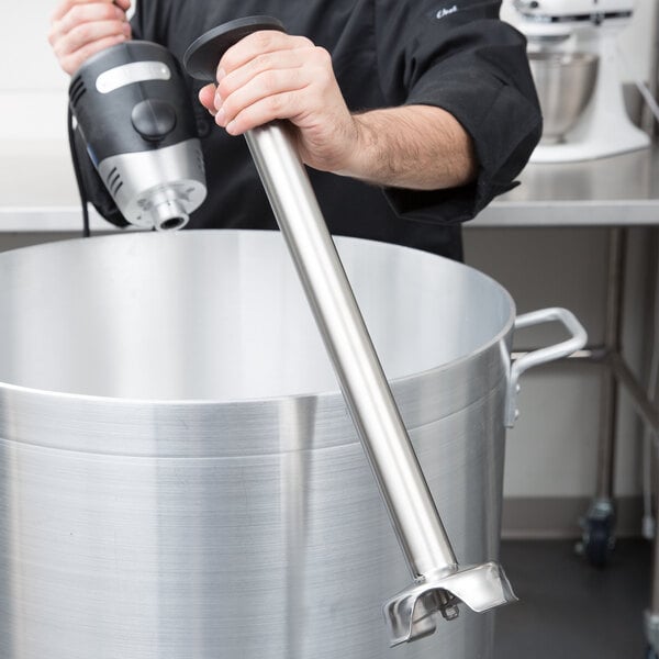 A man using a Waring stainless steel shaft to mix a large pot.