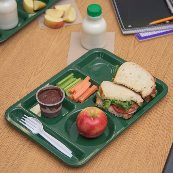 A Carlisle forest green 6 compartment tray with a sandwich, apple, and vegetables on it.
