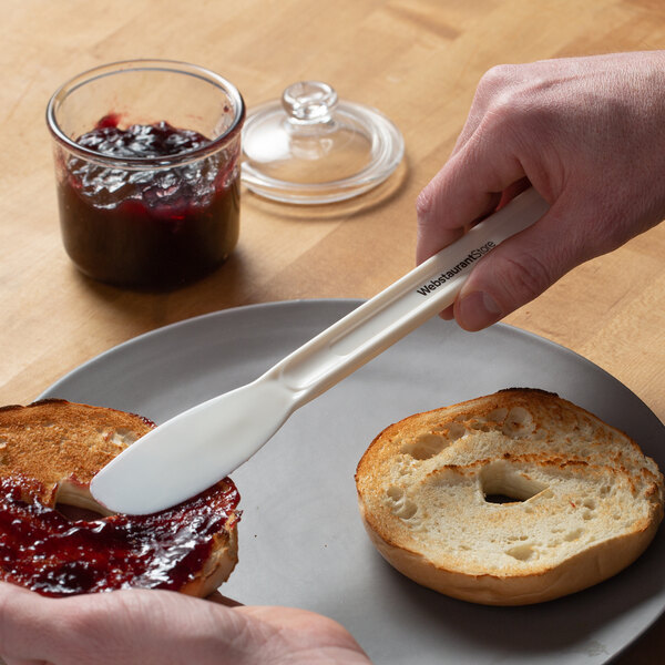 A person using a Choice Sandwich Spreader to spread jam on a piece of toasted bread.