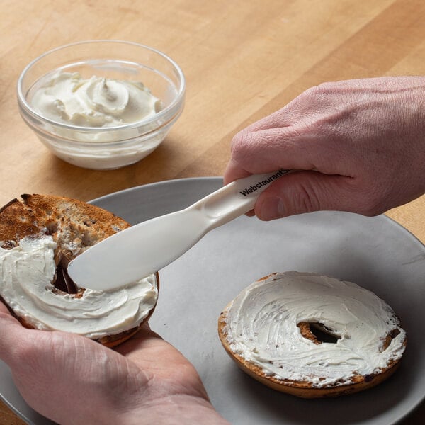 A person using a Choice sandwich spreader to spread cream on a bagel.