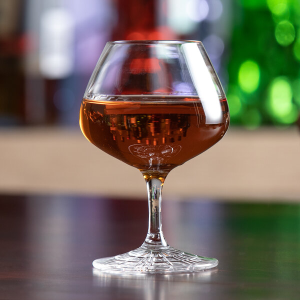 A Spiegelau Perfect Serve nosing glass filled with brown liquid on a table.