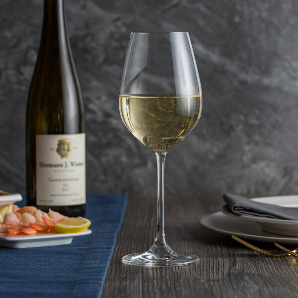 A Spiegelau white wine glass filled with white wine sits on a table next to a bottle of shrimp.