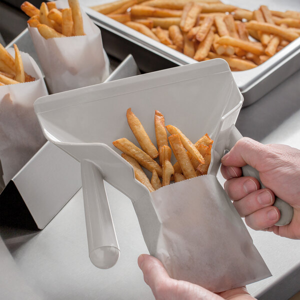 A person using a Vollrath dual handle French fry scoop to fill a bag with fries.