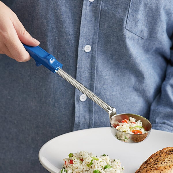 A hand holding a Vollrath blue stainless steel Spoodle over a plate of rice and vegetables.