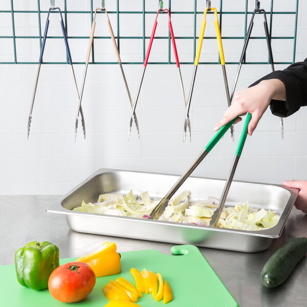 A hand with a green Vollrath Jacob's Pride tongs holding food on a tray.