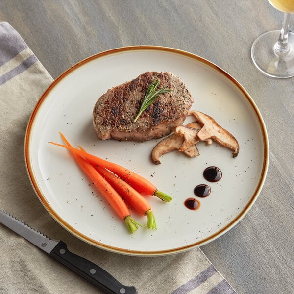 A plate of food with steak, mushrooms, and carrots on an Acopa Keystone vanilla bean stoneware coupe plate with a knife and a glass of wine.