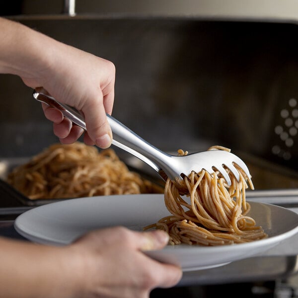 A person holding a Vollrath stainless steel spaghetti tong over a plate of noodles.