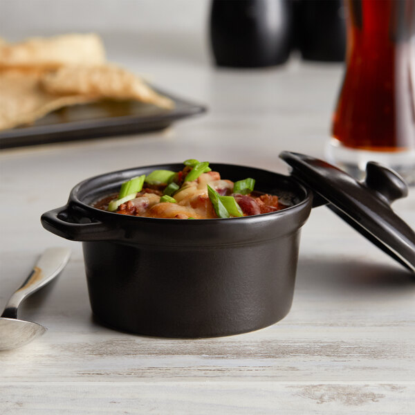 A black Acopa Keystone mini casserole dish with food in it and a lid.