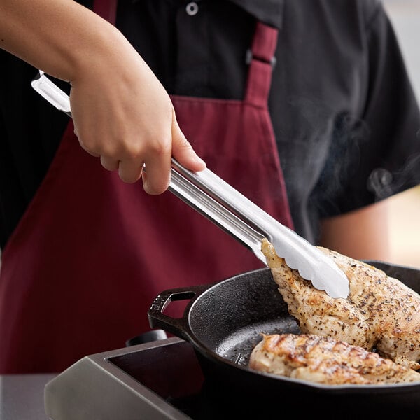 A person using Vollrath Jacob's Pride stainless steel tongs to cook food in a pan.