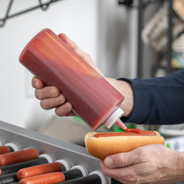 A hand using a Tablecraft squeeze bottle to pour ketchup onto a hot dog.
