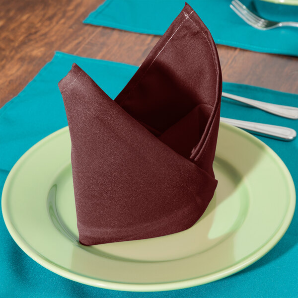 A folded Intedge burgundy cloth napkin on a plate.