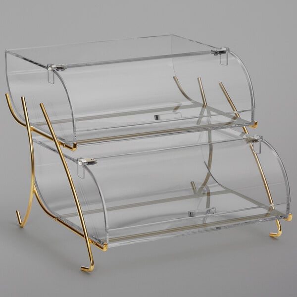 A clear acrylic pastry display case with brass wire legs.