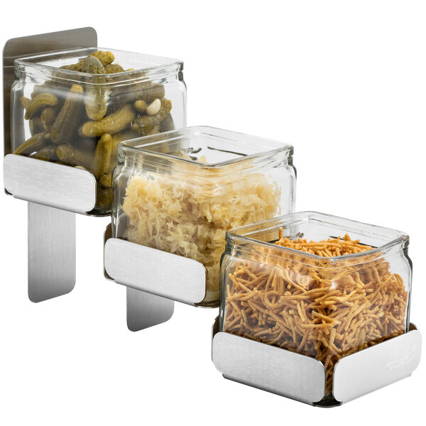 A Rosseto stainless steel condiment station with three glass containers of food on a counter.