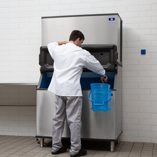 A man in a white shirt looking at a blue Manitowoc ice bucket in a freezer.