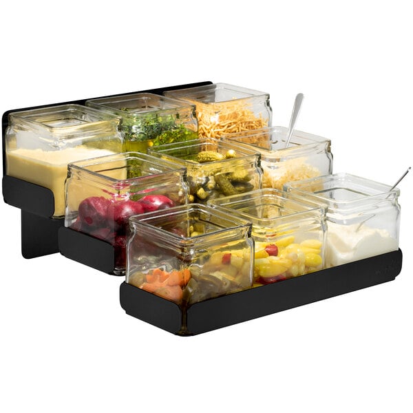 A Rosseto matte black 3-level condiment station with glass jars filled with different toppings on a counter.