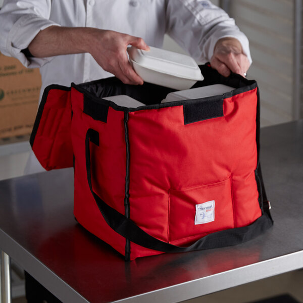 A man putting food into a red Cambro insulated bag with a white container.