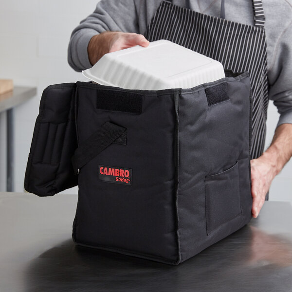 A person putting a white food container into a black Cambro GoBag.