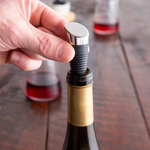 A hand using a Franmara Zocco rubber and chrome bottle stopper to open a bottle of wine.