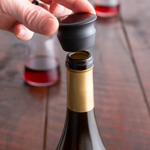 A hand using a Franmara Super Flex Seal Black Wine Stopper to close a bottle of wine.