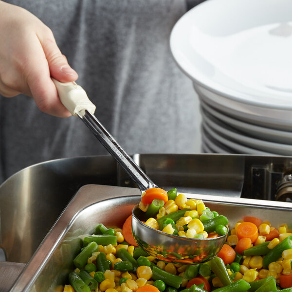 A hand using a Vollrath Ivory Perforated Spoodle to serve vegetables.