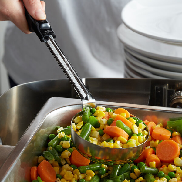 A person using a Vollrath black perforated portion spoon to serve vegetables.