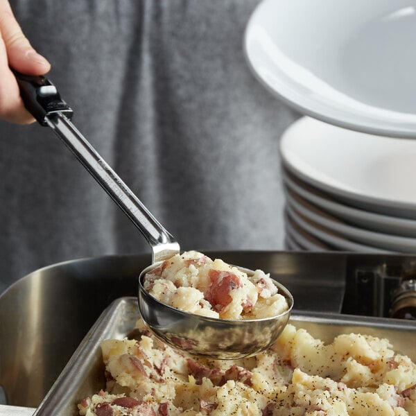 A person using a Vollrath black stainless steel spoodle to serve mashed potatoes.