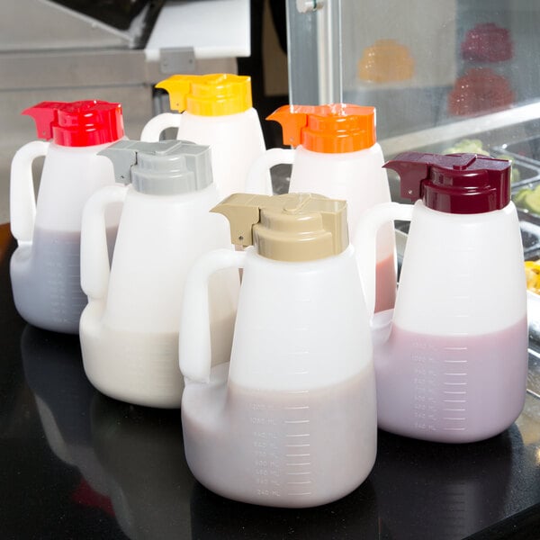 A group of Tablecraft plastic jugs with assorted colored lids on a counter.