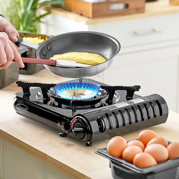 A person cooking eggs on a Sterno butane countertop range.