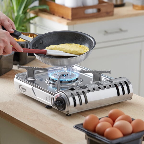 A person cooking eggs on a Sterno stainless steel butane countertop range.