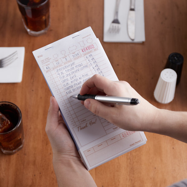 A person holding a pen and writing on a Choice tan and white guest check.