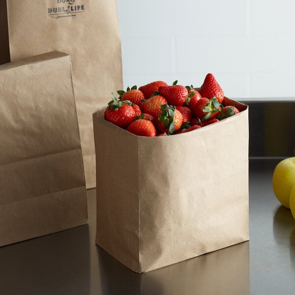 A Duro heavy-duty brown paper bag on a counter with a bowl of strawberries inside.
