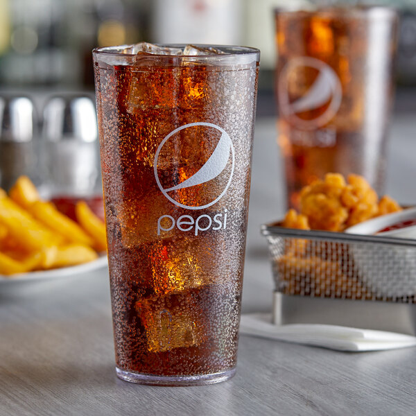 A clear plastic tumbler with Pepsi and ice on a table with a basket of chicken.