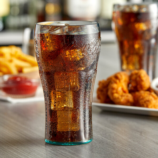 A jade plastic Coca-Cola glass filled with soda and ice on a table with chicken wings.