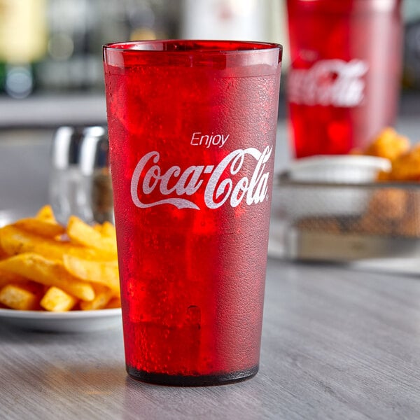 A close up of a red GET Coca-Cola tumbler filled with red liquid on a table with fries.
