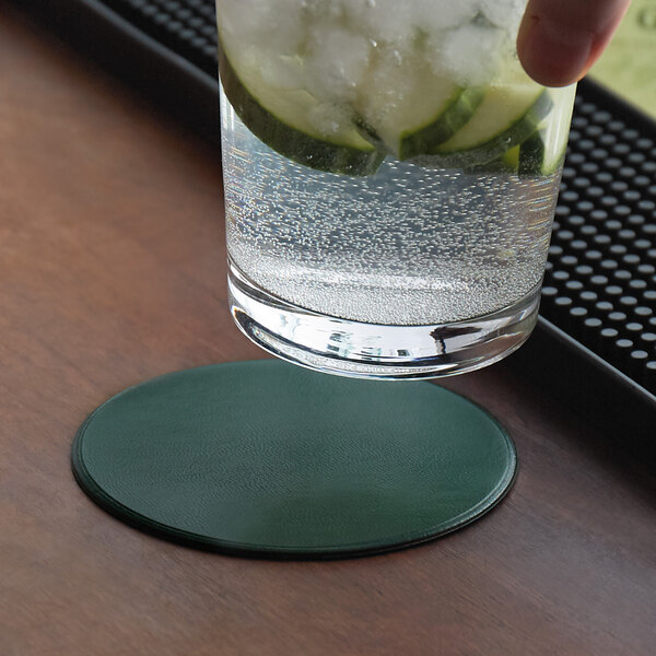 A hand holding a glass of water with a H. Risch, Inc. green vinyl coaster with cucumbers