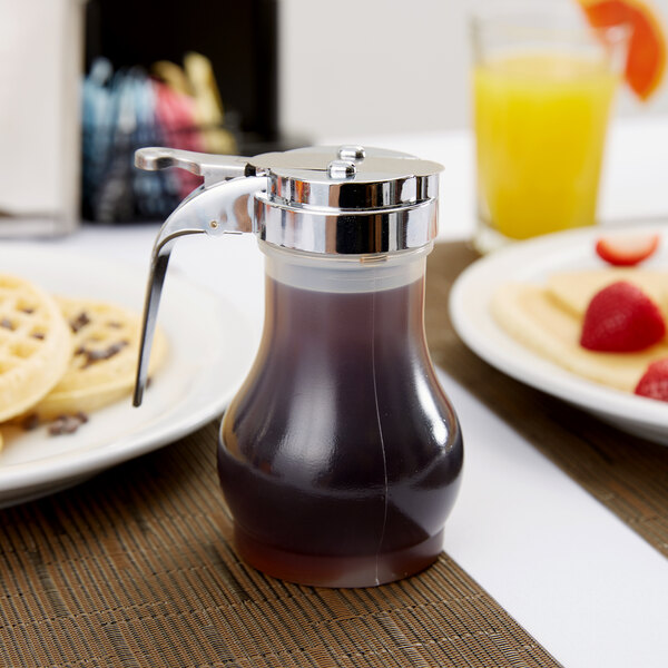 A Tablecraft syrup dispenser with a chrome lid on a table with waffles and orange juice.