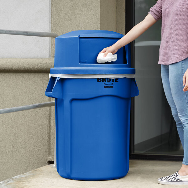 A woman using a blue Rubbermaid BRUTE trash can to throw away a tissue.
