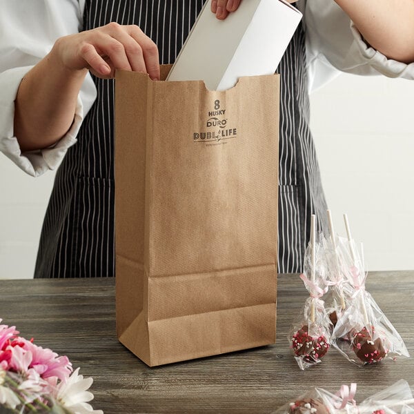 A woman putting a white box into a Duro brown paper bag with black text.