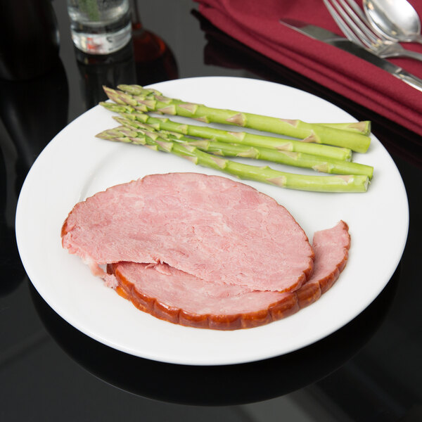 A Tuxton Alaska bright white china plate with sliced ham and asparagus on it.